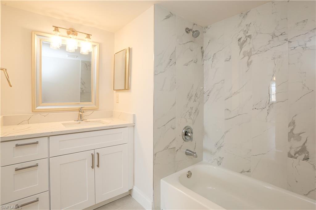 1265 Wildwood Lakes Boulevard, Unit 3306 Naples, FL 34104 - Photo 24 of 39 a bathroom with a granite countertop sink a mirror a bathtub and shower