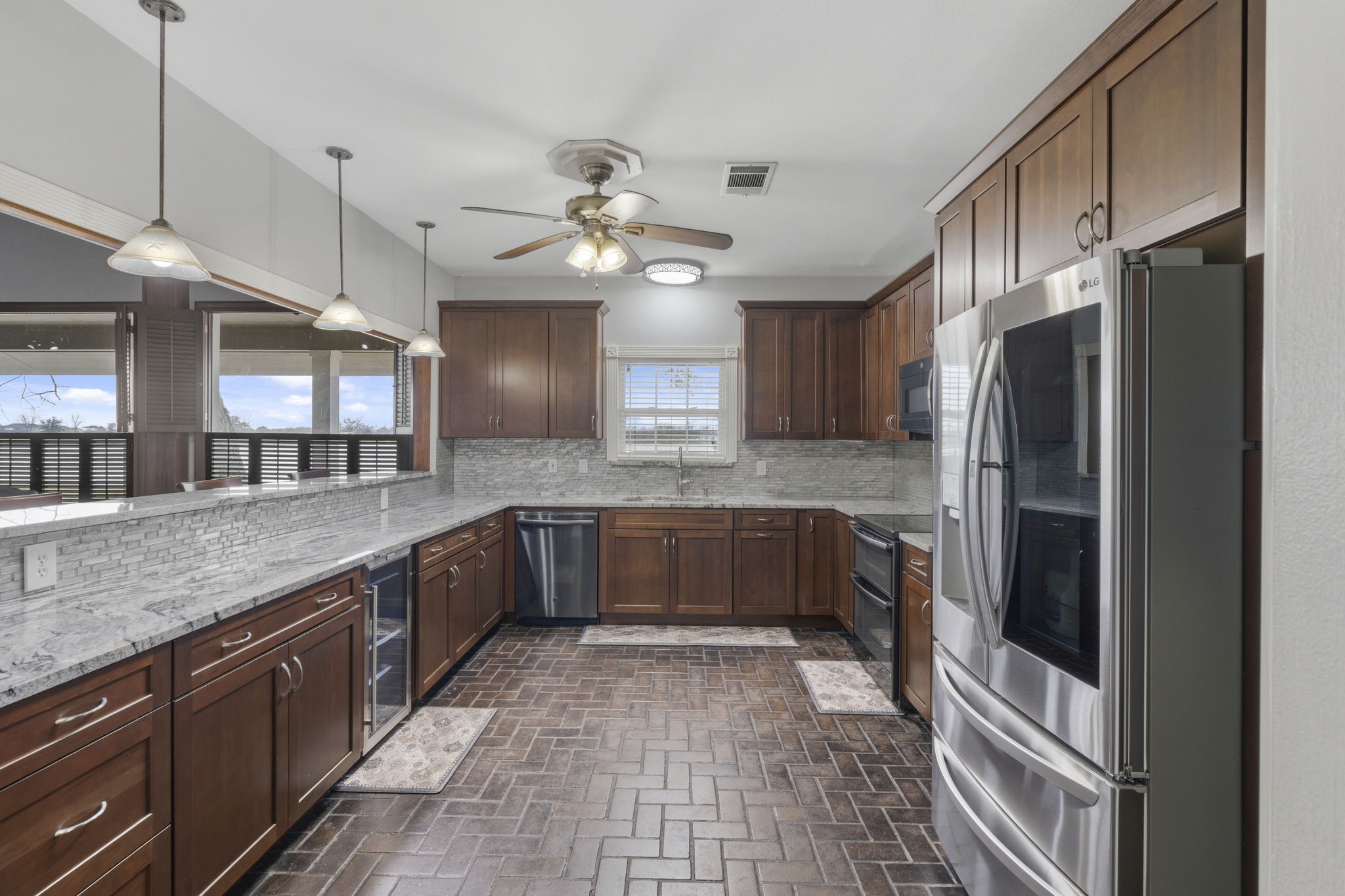 2935 West Fm 1462 Rosharon, TX 77583 - Photo 15 of 50 This well-appointed ranch kitchen blends classic craftsmanship with everyday functionality, designed to serve as a true working heart of the home. Rich wood cabinetry provides ample storage, while durable stone countertops and a tile backsplash offer both beauty and easy maintenance. With its practical design and warm finishes, this kitchen is built for gathering, cooking, and supporting the rhythm of life on the land.