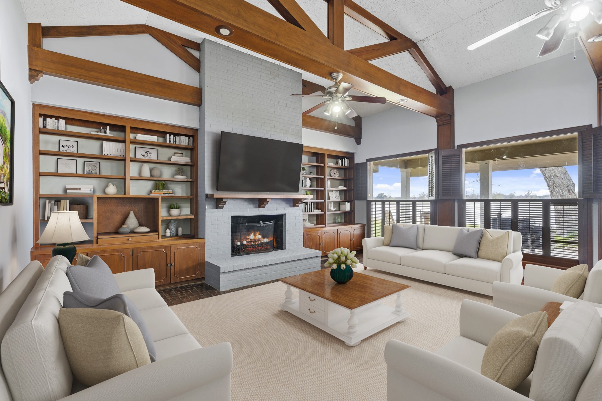 2935 West Fm 1462 Rosharon, TX 77583 - Photo 18 of 50 Virtually Staged: This ranch living room blends classic craftsmanship with inviting comfort, anchored by a brick fireplace that serves as a natural focal point. Exposed wood beams and trusses soar overhead, adding architectural strength and a timeless ranchhouse feel, while ceiling fans and large windows keep the space light and breezy. Custom built-in shelving and cabinetry provide both character and practical storage, framing the fireplace with warm wood tones.