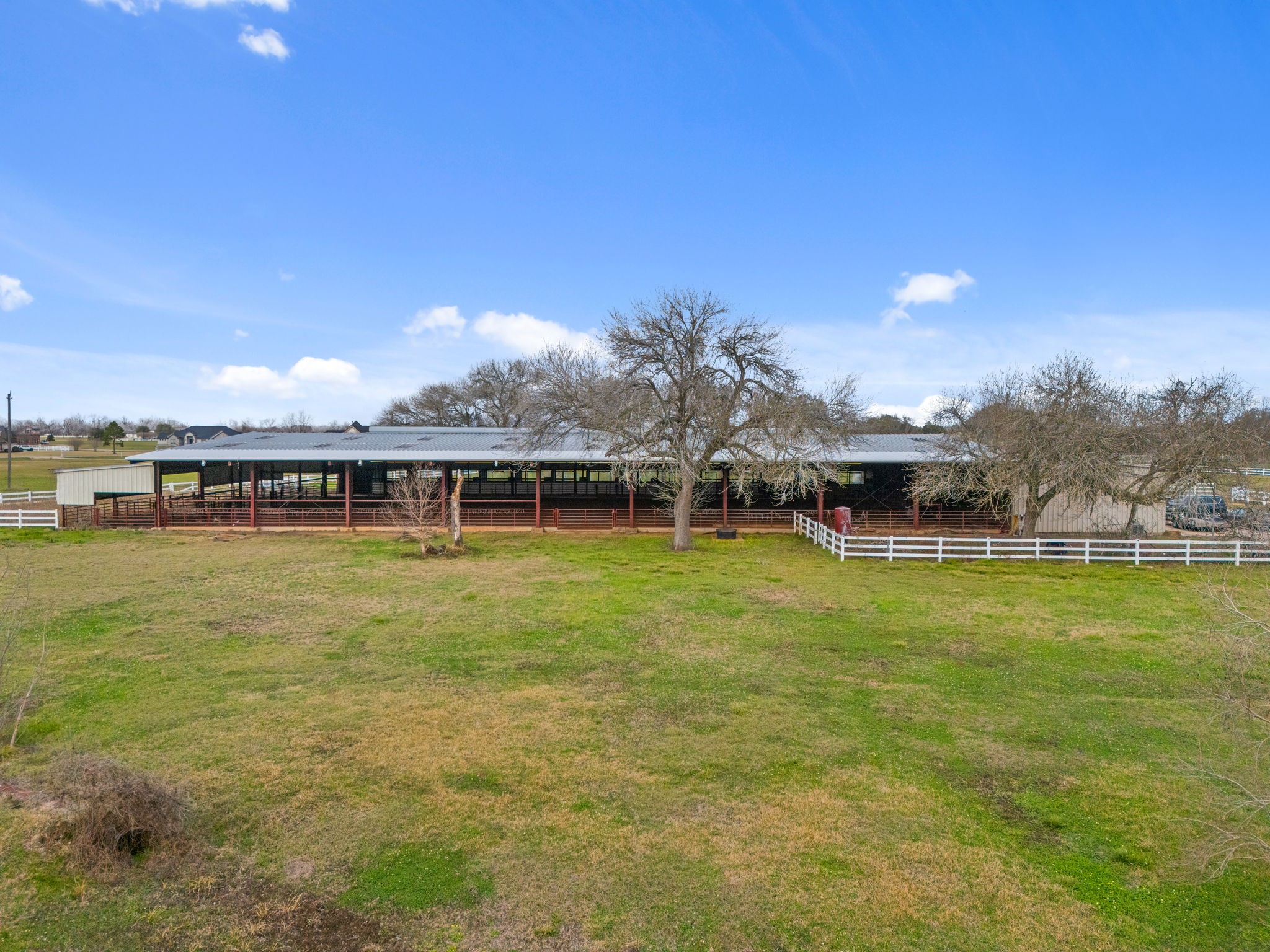 2935 West Fm 1462 Rosharon, TX 77583 - Photo 2 of 50 This wide, open view showcases a well-established ranch setting with expansive pastureland and a large covered livestock or equipment structure stretching across the property. The long, open-sided building provides ample shelter and airflow, ideal for livestock, hay storage, or ranch operations.