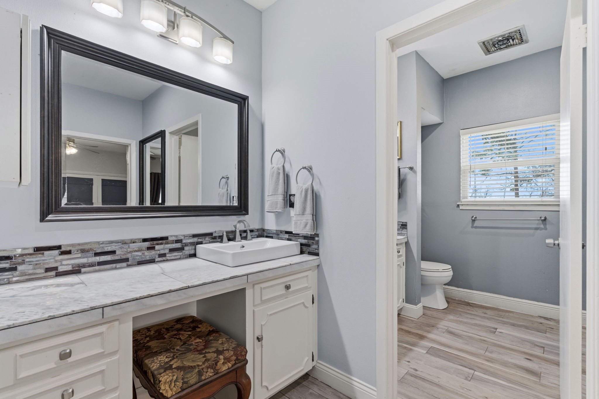 2935 West Fm 1462 Rosharon, TX 77583 - Photo 23 of 50 This photo shows a bright, well-designed bathroom vanity area that blends style with function. A large framed mirror and modern light fixture illuminate the space, highlighting the white cabinetry and tile-topped counter with a sleek rectangular sink. An open knee space beneath the vanity adds flexibility and convenience.