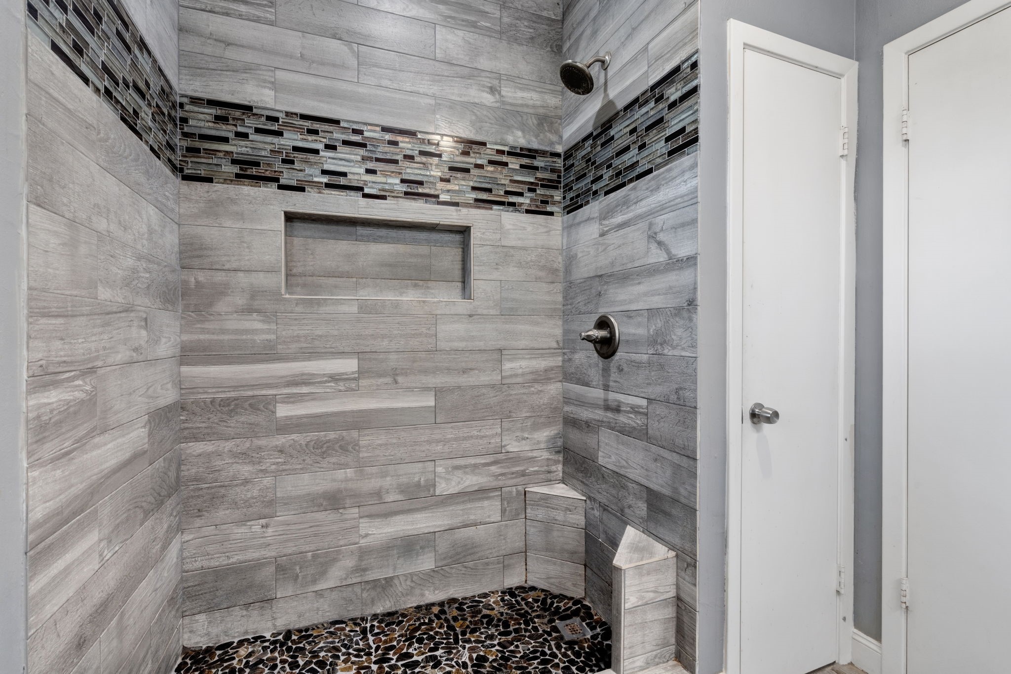 2935 West Fm 1462 Rosharon, TX 77583 - Photo 25 of 50 This photo shows a beautifully updated walk-in shower with a clean, modern design. The walls are finished in large-format, wood-look tile laid horizontally, accented by a decorative mosaic tile band for added texture and visual interest.