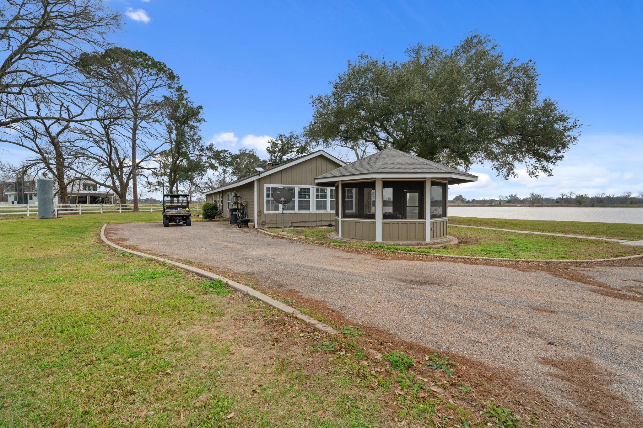 2935 West Fm 1462 Rosharon, TX 77583 - Photo 30 of 50 This charming ranch-side scene showcases a thoughtfully designed outbuilding set along a curved gravel drive, blending functionality with scenic appeal. A screened gazebo-style structure sits prominently in the foreground, offering a peaceful spot to relax while taking in sweeping views of the nearby lake.