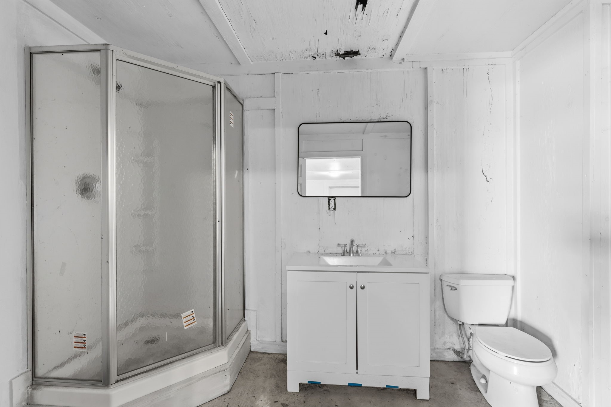 2935 West Fm 1462 Rosharon, TX 77583 - Photo 33 of 50 This image shows a simple, utilitarian bathroom with a straightforward ranch-style layout. The space includes a corner glass-enclosed shower, a compact white vanity with sink and mirror, and a standard toilet positioned to the side.