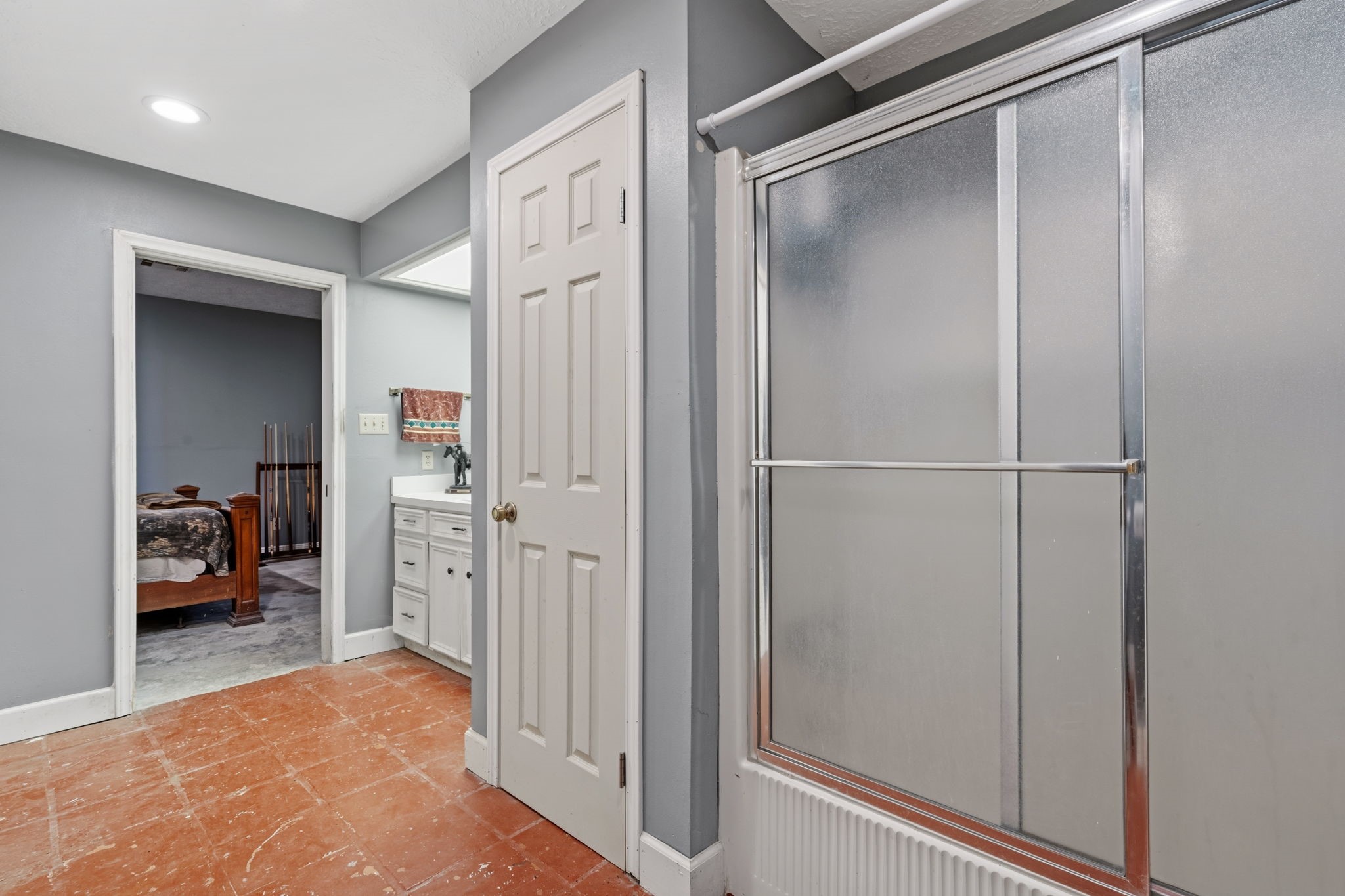 2935 West Fm 1462 Rosharon, TX 77583 - Photo 37 of 50 This photo shows a clean, functional bathroom area with a practical layout. The space features terracotta-style tile flooring that adds durability and character, paired with soft gray walls and crisp white trim. A glass-enclosed shower with a sliding door sits to the right, offering a simple, low-maintenance design.