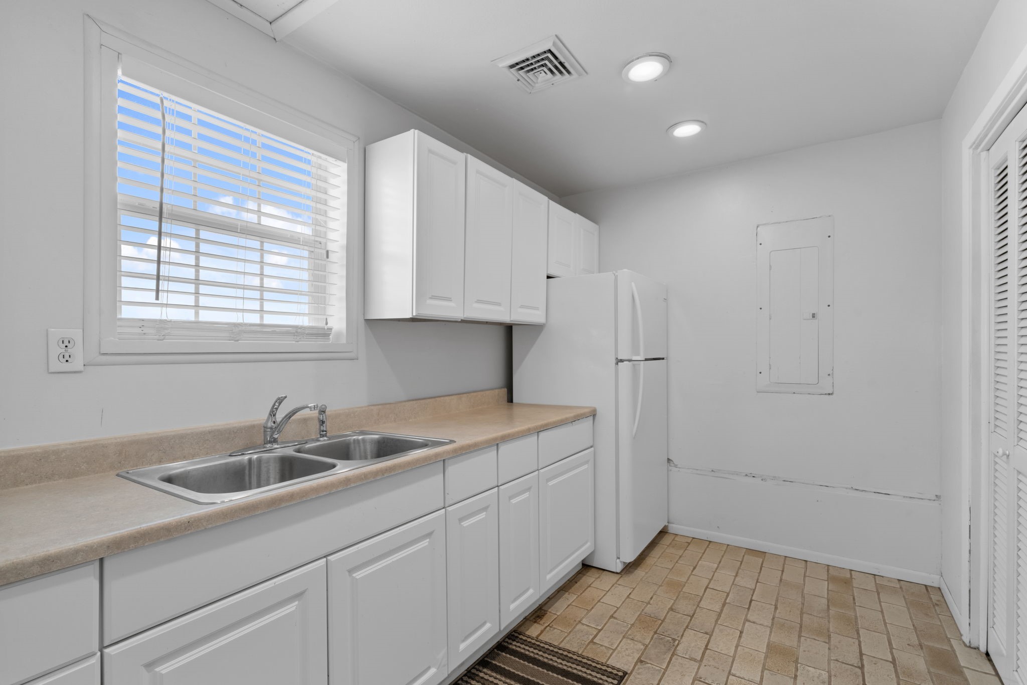 2935 West Fm 1462 Rosharon, TX 77583 - Photo 44 of 50 This photo shows a clean, functional kitchen area with a bright, minimalist design. White cabinetry lines the wall, paired with light countertops and a double-basin sink beneath a window that brings in natural light