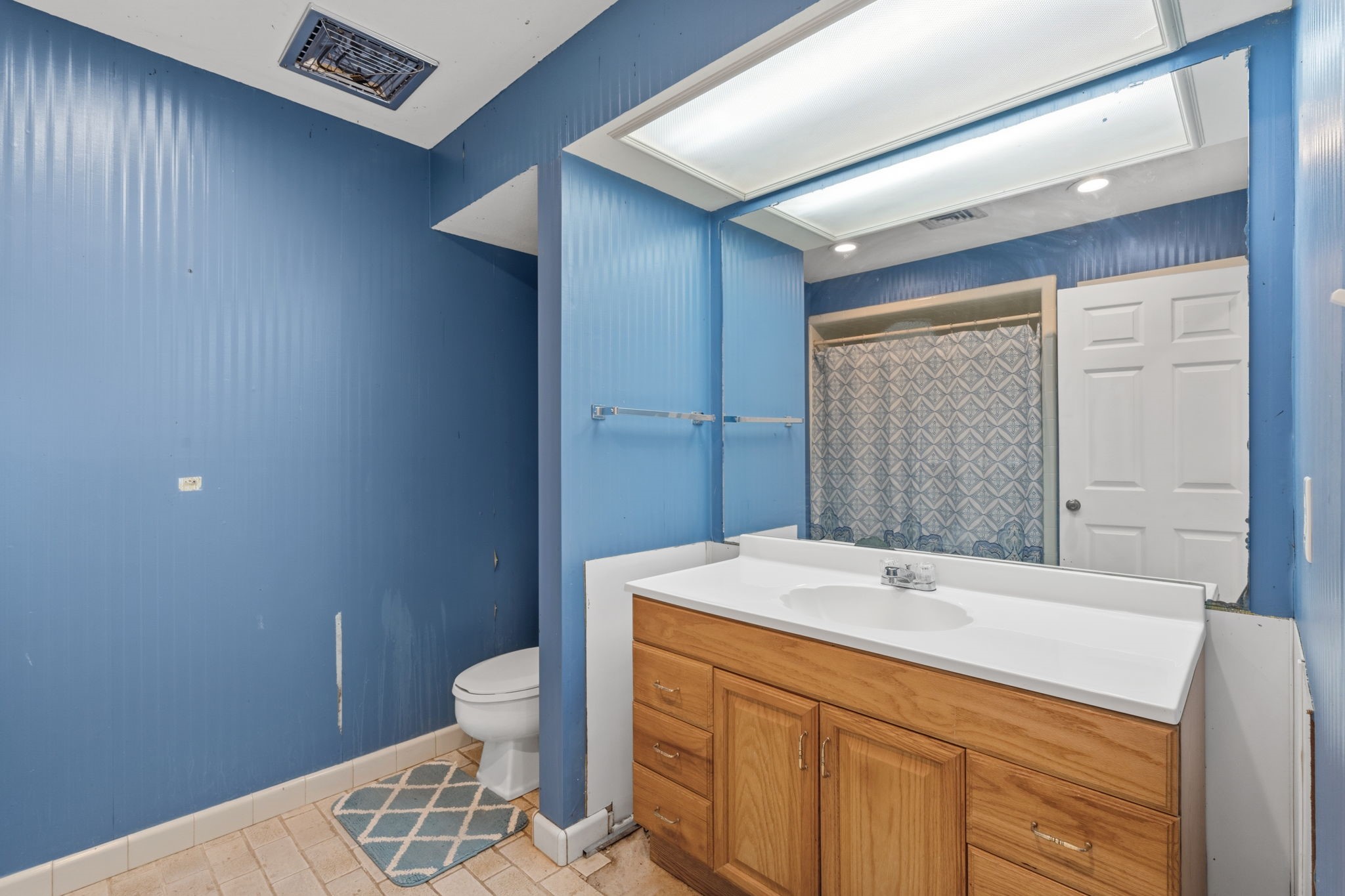 2935 West Fm 1462 Rosharon, TX 77583 - Photo 46 of 50 This bathroom offers a functional layout with a single-sink vanity featuring a solid countertop and warm wood cabinetry. A large mirror with overhead lighting brightens the space, while the blue paneled walls add character and contrast.