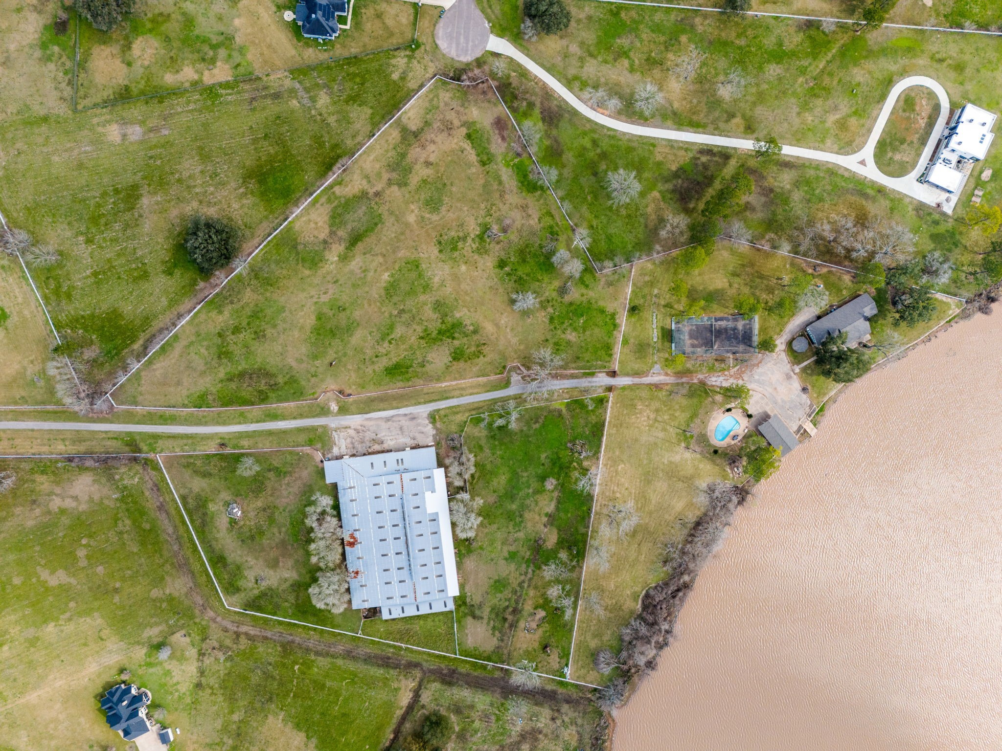 2935 West Fm 1462 Rosharon, TX 77583 - Photo 48 of 50 Beyond the court, the main ranch home sits comfortably near the water, with the pool and pool house positioned along the shoreline for easy outdoor enjoyment.