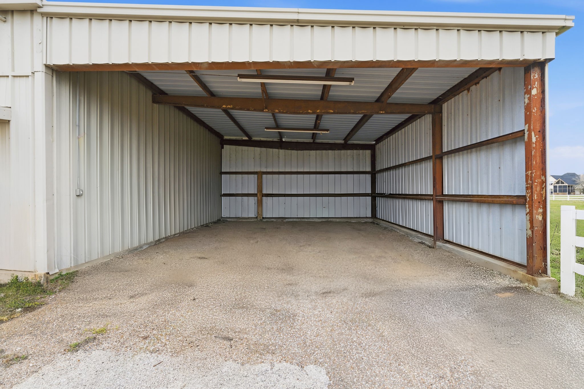 2935 West Fm 1462 Rosharon, TX 77583 - Photo 49 of 50 This open-sided metal structure offers practical, no-nonsense storage well suited for ranch use. Built with durable steel framing and corrugated metal panels, it provides ample covered space for parking equipment, trailers, ATVs, or storing feed and ranch supplies. The wide opening allows for easy drive-through access, while the gravel floor keeps maintenance simple and functional. Overhead lighting adds visibility for early mornings or late evenings, making this a versatile outbuilding.