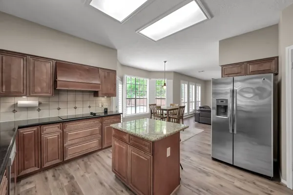 a kitchen with granite countertop stainless steel appliances a sink dishwasher a refrigerator and cabinets with wooden floor