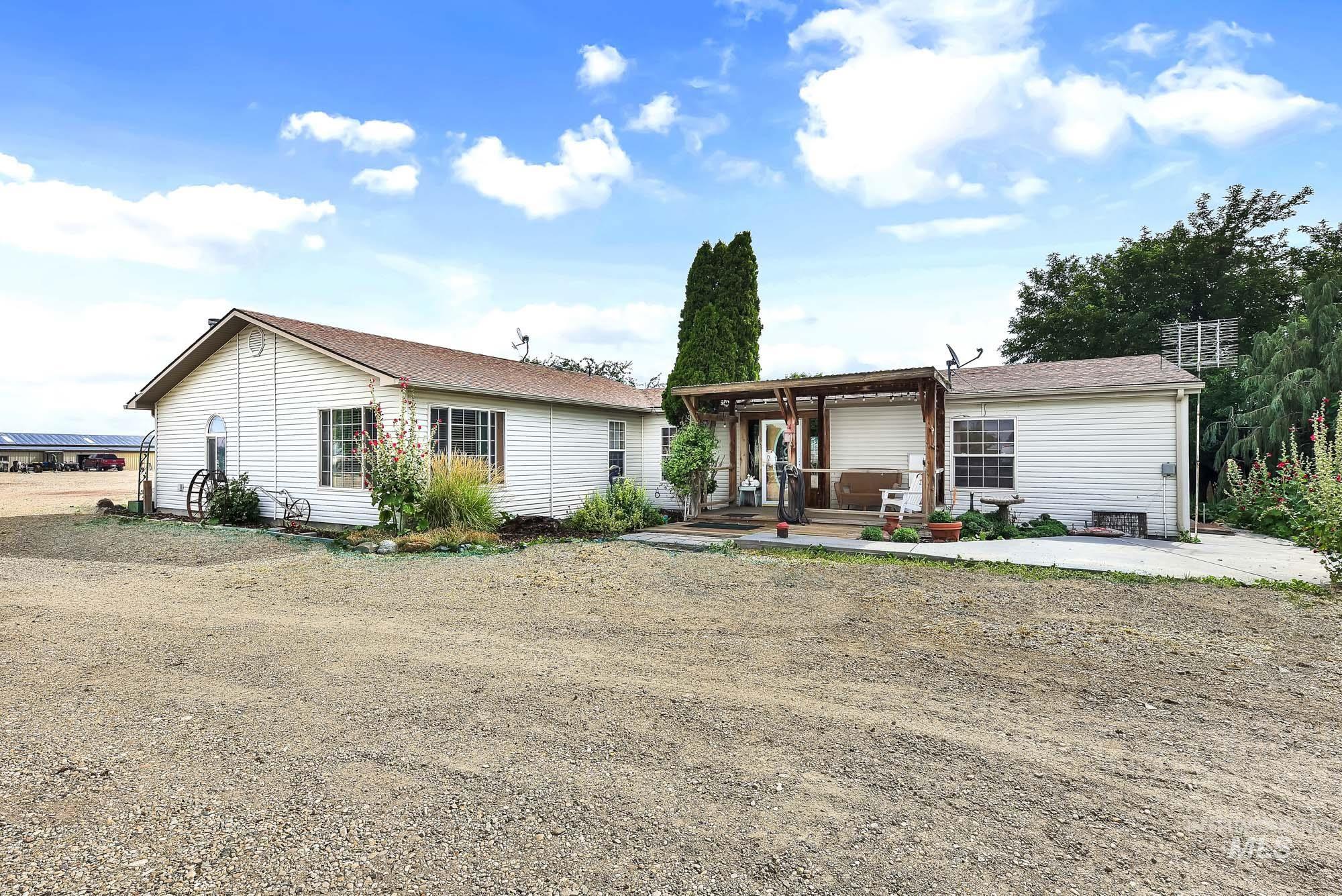 24900 Market Road Parma, ID 83660 - Photo 3 of 50 White-sided residential structure with a brown shingle roof, featuring multiple windows and an attached covered patio with a wood pergola