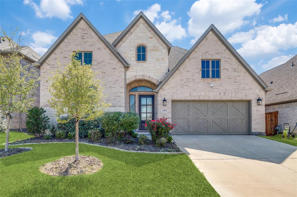 French country inspired facade with brick siding, driveway, a garage, a front lawn, and stone siding