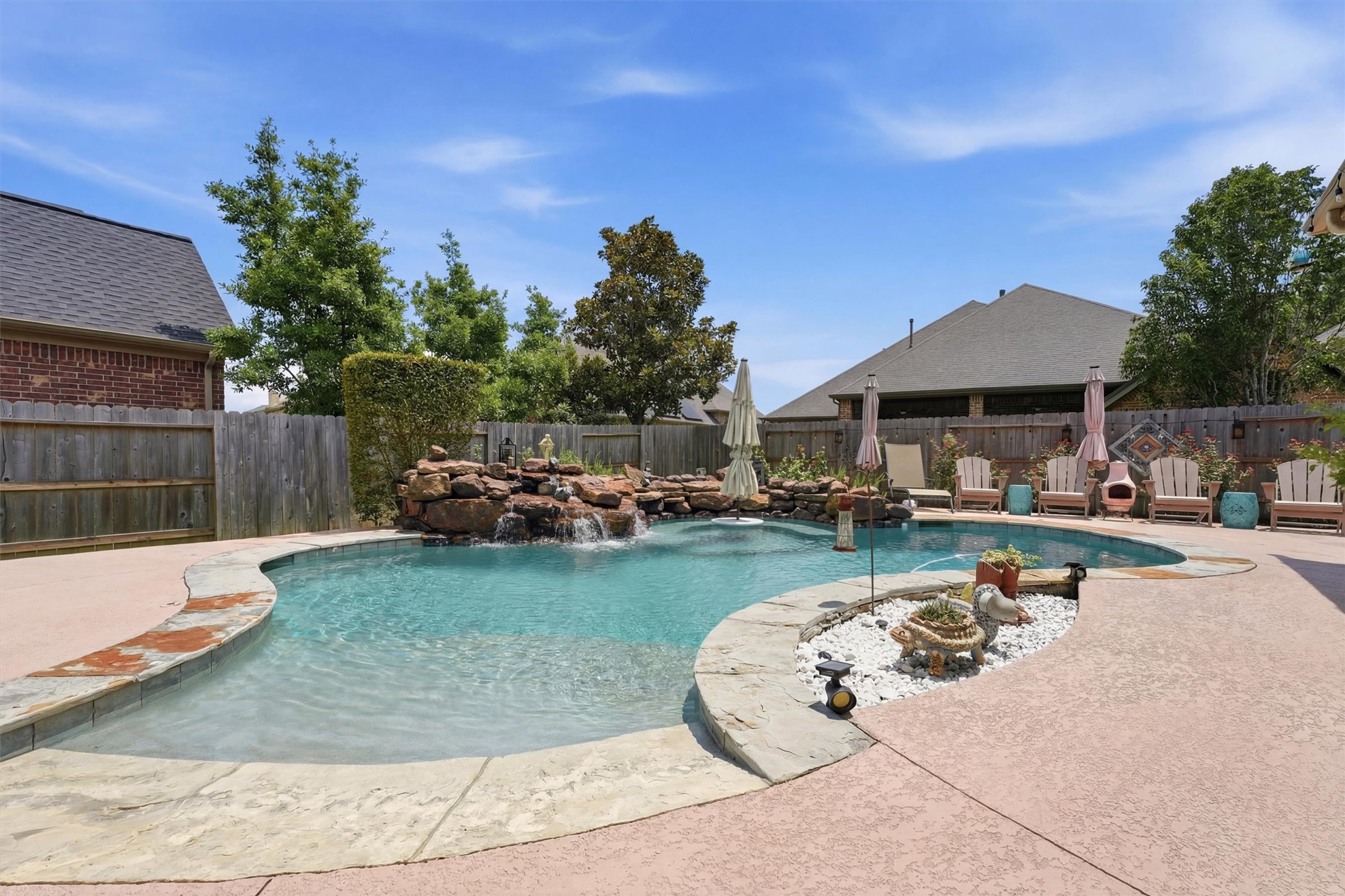 17710 Rough River Court Humble, TX 77346 - Photo 27 of 38 This backyard features a spacious in-ground pool with a waterfall, surrounded by a stone patio. There are several seating areas with umbrellas, and the space is enclosed by a wooden fence, offering privacy and a great spot for relaxation or entertaining.