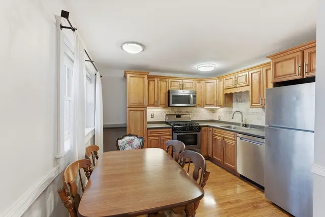 a kitchen with stainless steel appliances granite countertop a refrigerator a sink dishwasher a stove a dining table and chairs with wooden floor