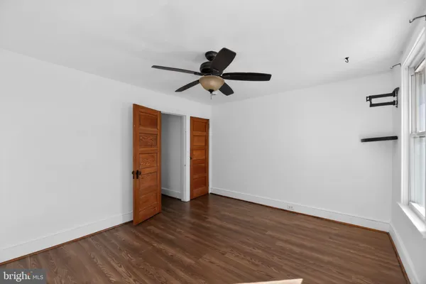 a view of an empty room with wooden floor and a ceiling fan