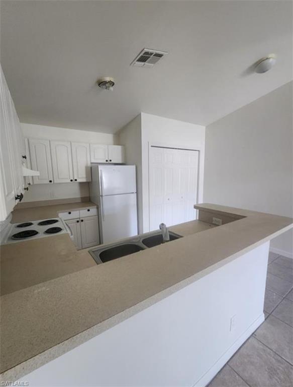 1854 55th Terrace Southwest Naples, FL 34116 - Photo 2 of 9 Kitchen with white appliances, light countertops, light tile patterned floors, white cabinetry, and a peninsula