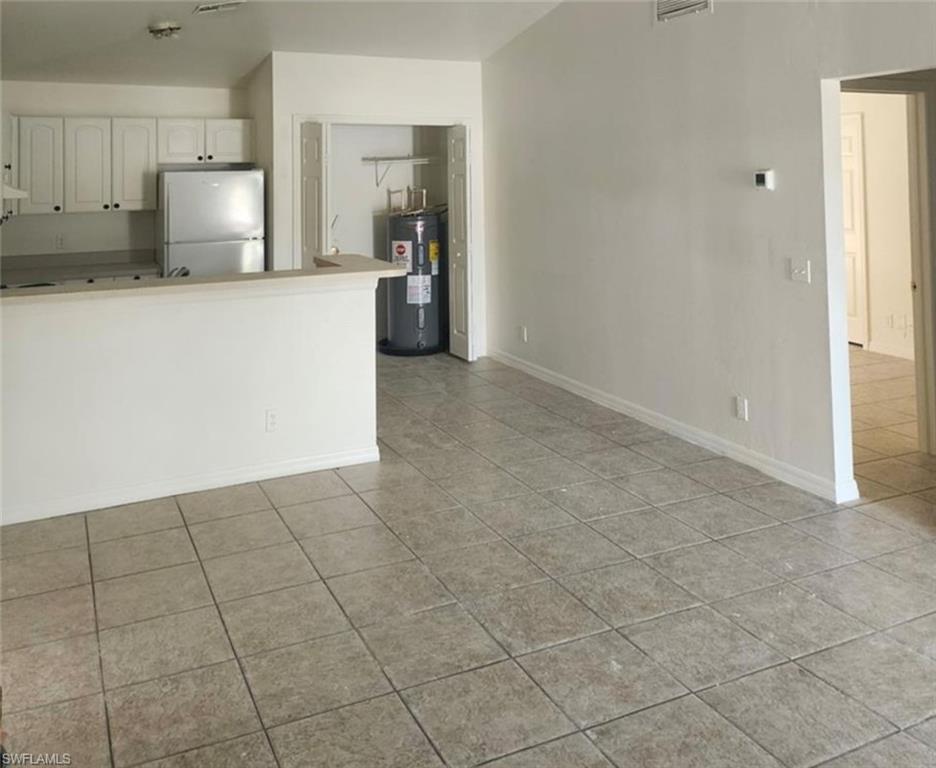 1854 55th Terrace Southwest Naples, FL 34116 - Photo 3 of 9 Kitchen with freestanding refrigerator, white cabinets, electric water heater, light tile patterned flooring, and a peninsula