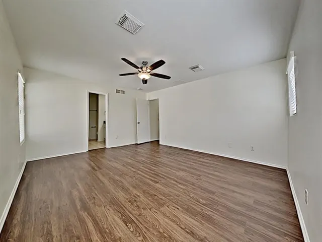 a view of an empty room with wooden floor and a ceiling fan