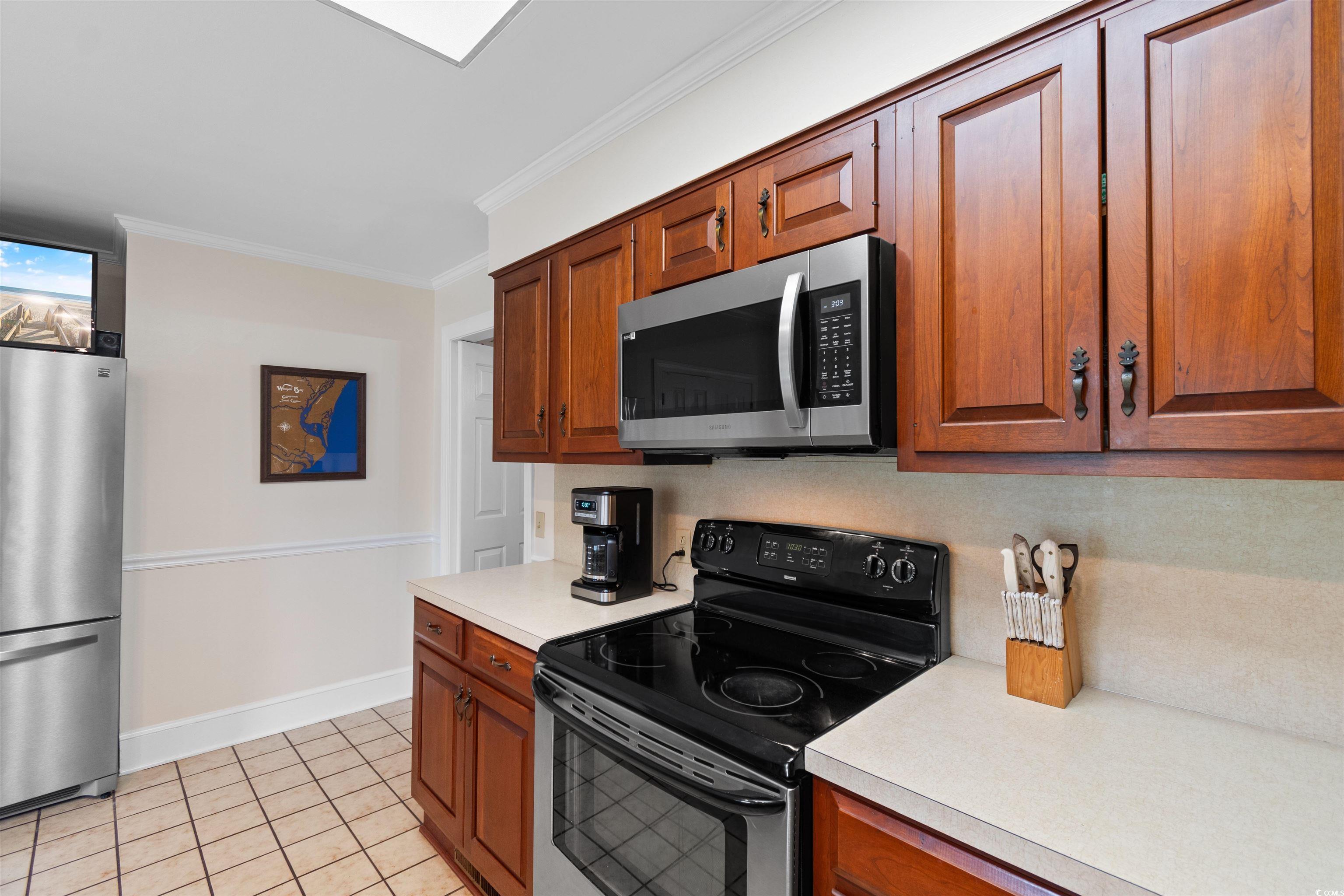 14 Live Oak Lane Georgetown, SC 29440 - Photo 7 of 40 Kitchen featuring stainless steel appliances, crown molding, light countertops, light tile patterned floors, and brown cabinets