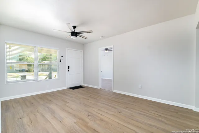 an empty room with wooden floor ceiling fan and windows