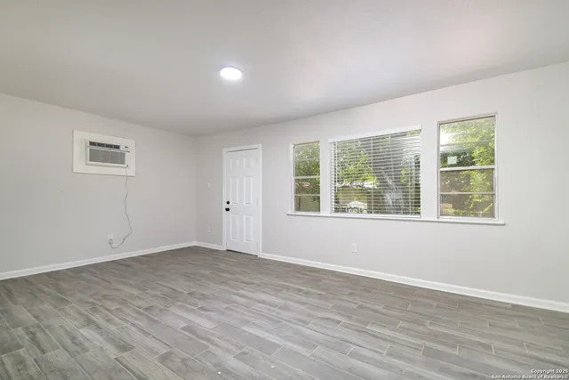 a view of an empty room with wooden floor and a window