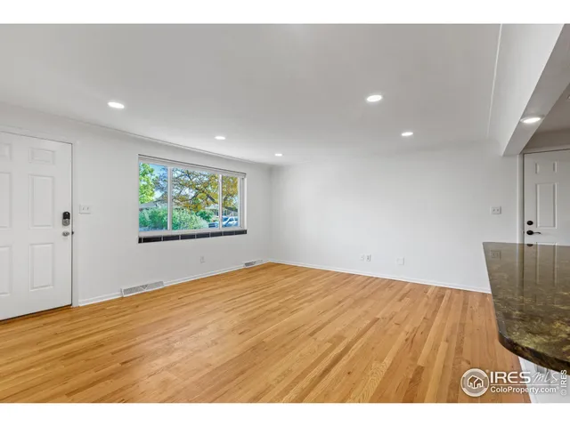 a view of an empty room with wooden floor and a ceiling fan