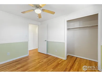 a view of an empty room with wooden floor and a ceiling fan