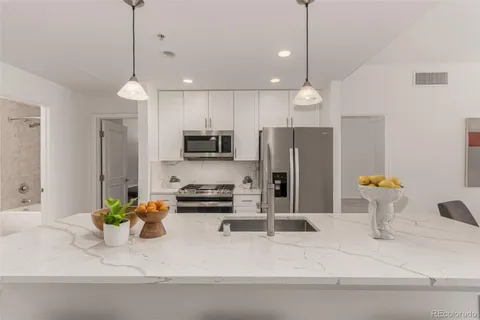 a kitchen with stainless steel appliances a refrigerator a sink a center island a stove cabinets and living room view