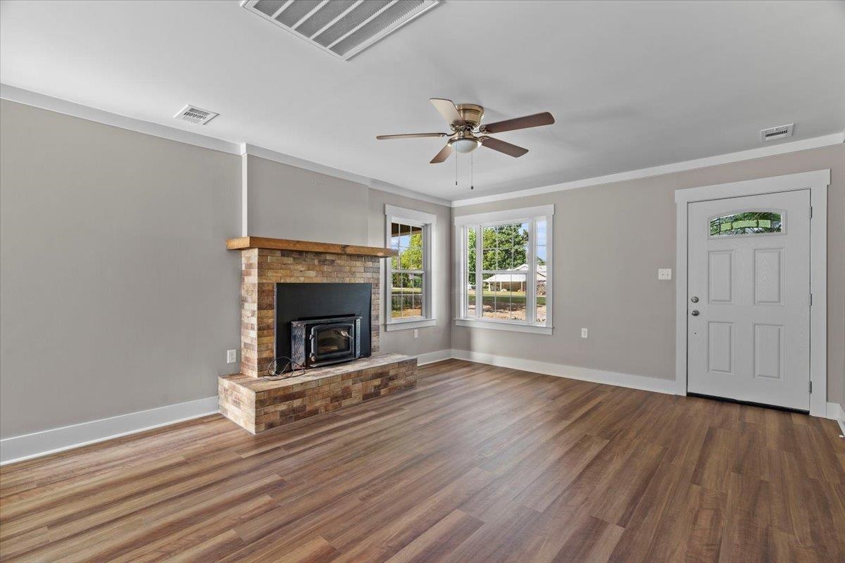 101 Sivil Circle Covington, TN 38019 - Photo 11 of 40 Unfurnished living room featuring dark wood-style floors, ornamental molding, a ceiling fan, and a wood stove