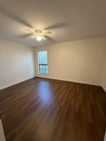 a view of an empty room with wooden floor and a ceiling fan