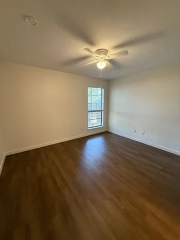 a view of an empty room with wooden floor and a ceiling fan