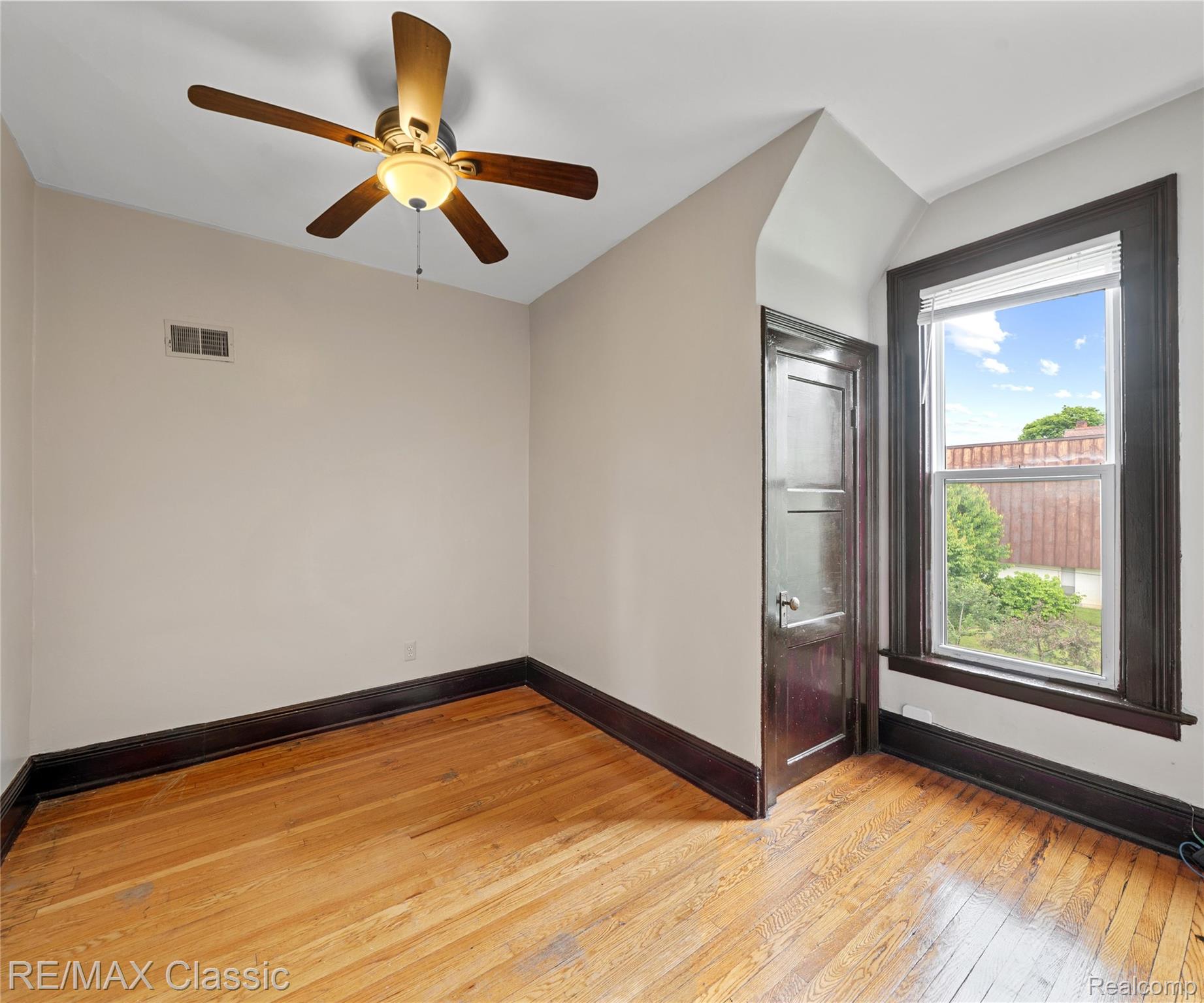 3941 Trumbull Detroit, MI 48208 - Photo 28 of 46 Room featuring wood-finish flooring, a ceiling fan with integrated lighting, a single window with blinds, a dark wood-finish door, and light-toned walls with dark trim