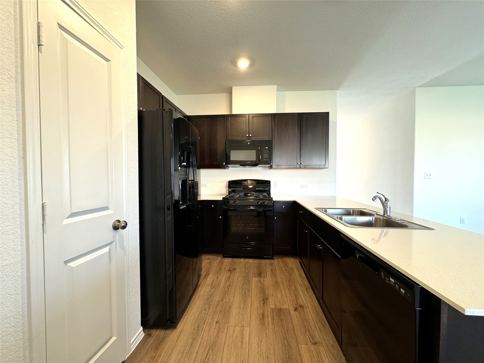 14408 Koti Way Pflugerville, TX 78660 - Photo 5 of 14 Kitchen featuring black appliances, light countertops, light wood-type flooring, a peninsula, and dark wood finish cabinets