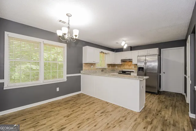 a kitchen with stainless steel appliances granite countertop a refrigerator a sink dishwasher a stove and white countertops with wooden floor