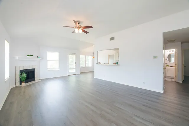 an empty room with wooden floor fireplace and windows