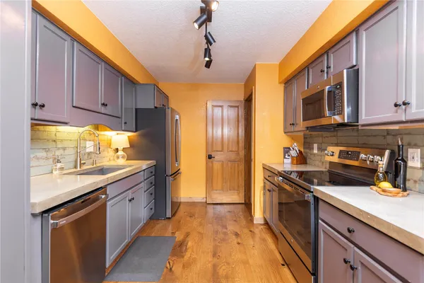 a kitchen with stainless steel appliances granite countertop a stove a sink dishwasher and a refrigerator with wooden cabinets