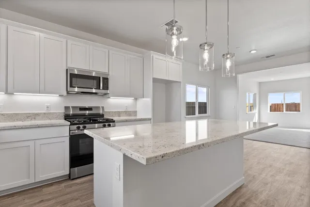 a large kitchen with granite countertop a stove a sink a center island a refrigerator and a stove top oven