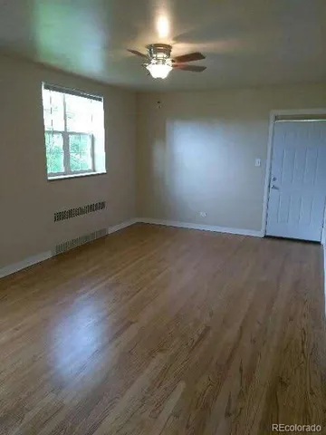 an empty room with wooden floor chandelier fan and windows