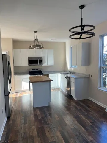 a kitchen with stainless steel appliances a microwave a stove a sink dishwasher a refrigerator and white cabinets with wooden floor