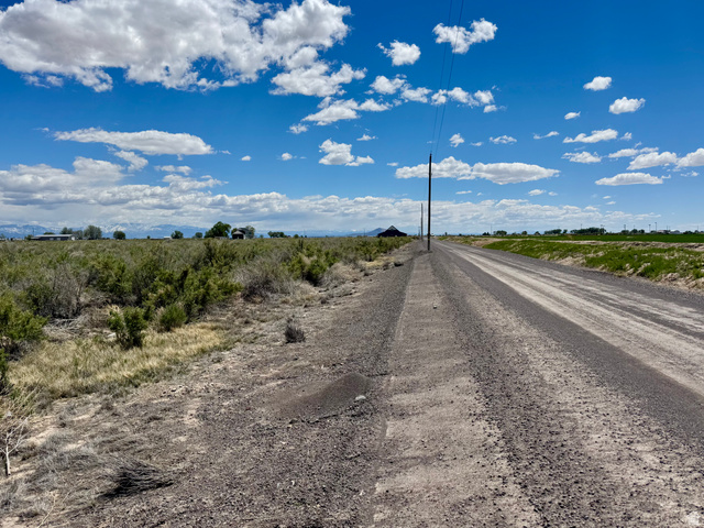 2225 South 500th Street East Delta, UT 84624 - Photo 1 of 9 Expansive rural landscape featuring a gravel road, open fields, and distant mountain ranges. 10.75 acres on the outskirts of Delta.