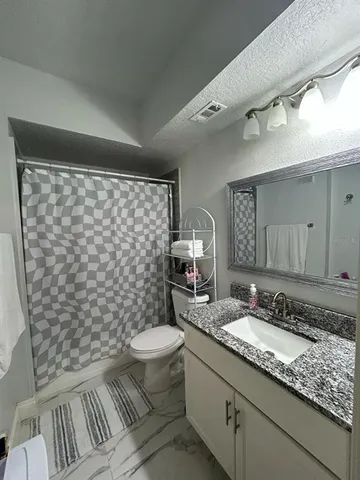 a bathroom with a granite countertop sink a toilet a mirror and shower curtain