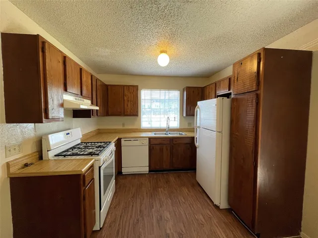a kitchen with a refrigerator a stove a sink dishwasher and wooden cabinets with wooden floor