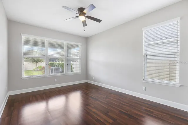 a view of an empty room with wooden floor and a ceiling fan