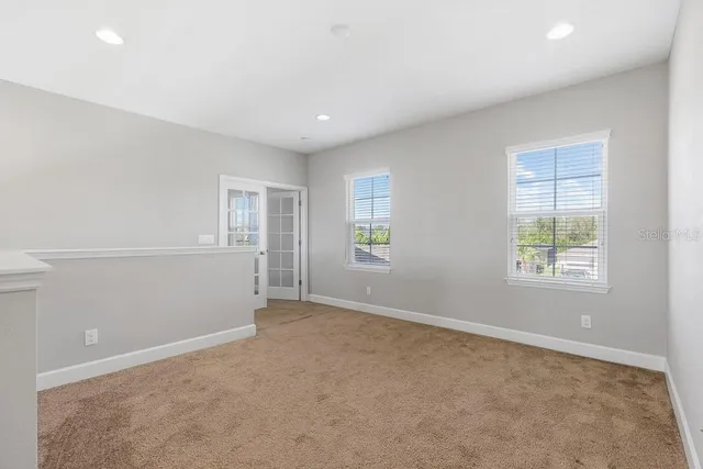 an empty room with chandelier fan and windows