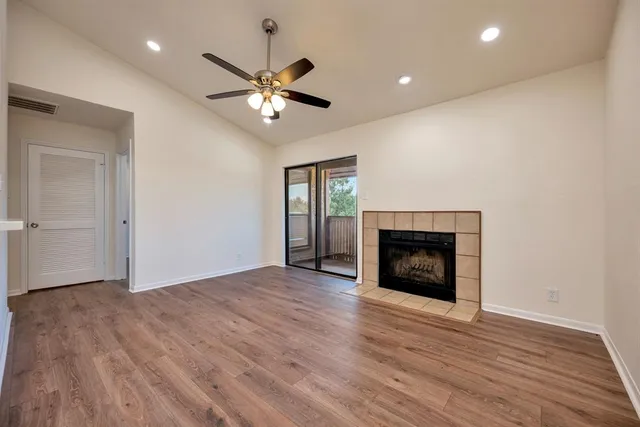 a view of an empty room with wooden floor fireplace and a window