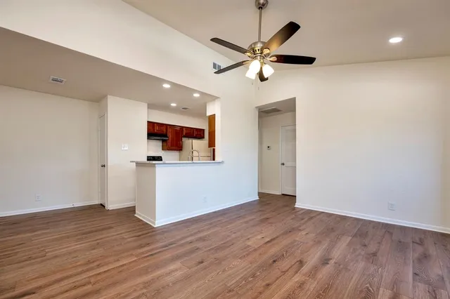 a view of a big room with wooden floor a ceiling fan and kitchen space