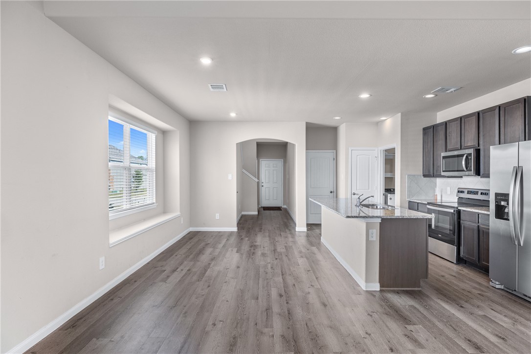 974 Harper Lane Bryan, TX 77803 - Photo 11 of 38 Kitchen with appliances with stainless steel finishes, arched walkways, an island with sink, light stone counters, and backsplash