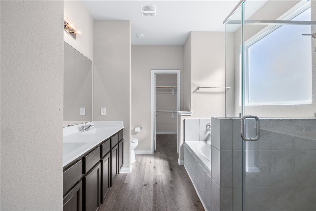 974 Harper Lane Bryan, TX 77803 - Photo 19 of 38 Bathroom featuring a bath, a spacious closet, dark wood-style floors, double vanity, and a shower stall