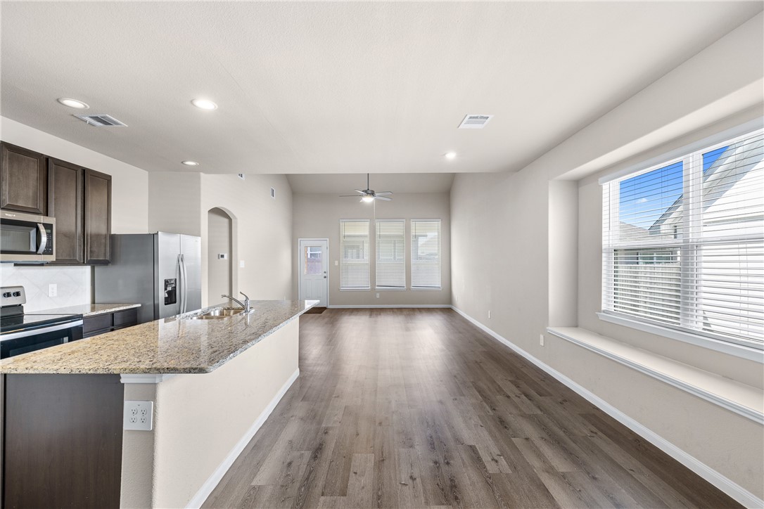 974 Harper Lane Bryan, TX 77803 - Photo 7 of 38 Kitchen with dark brown cabinets, light wood-type flooring, arched walkways, stainless steel appliances, and a kitchen island with sink