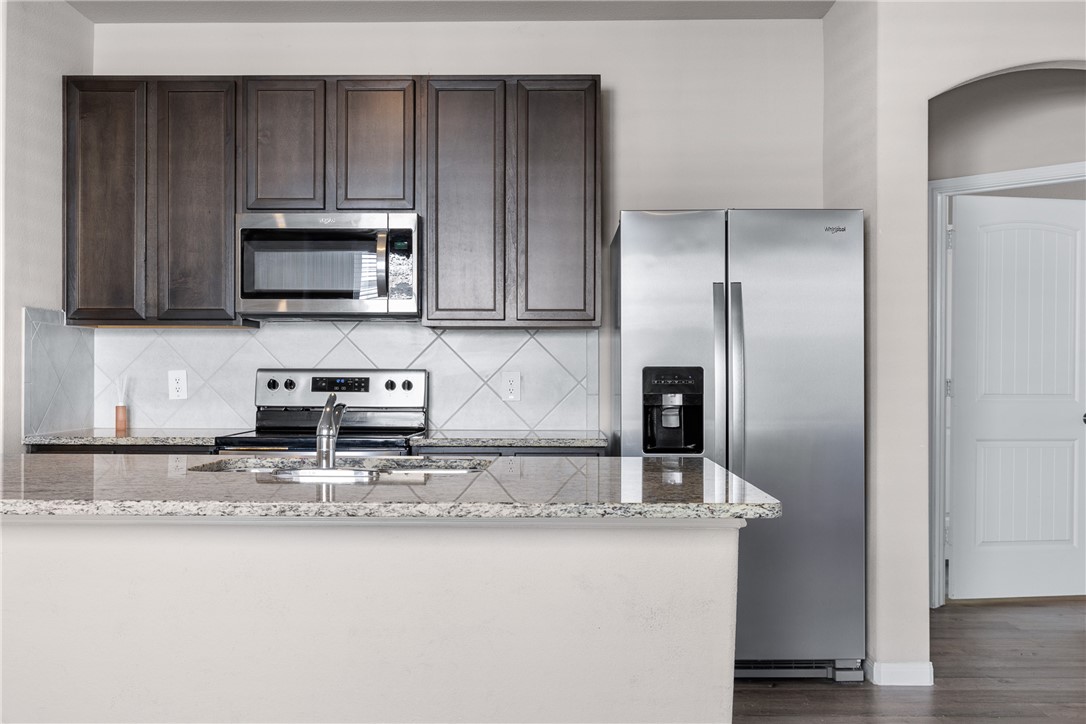 974 Harper Lane Bryan, TX 77803 - Photo 10 of 38 Kitchen with stainless steel appliances, light stone countertops, dark brown cabinets, and tasteful backsplash